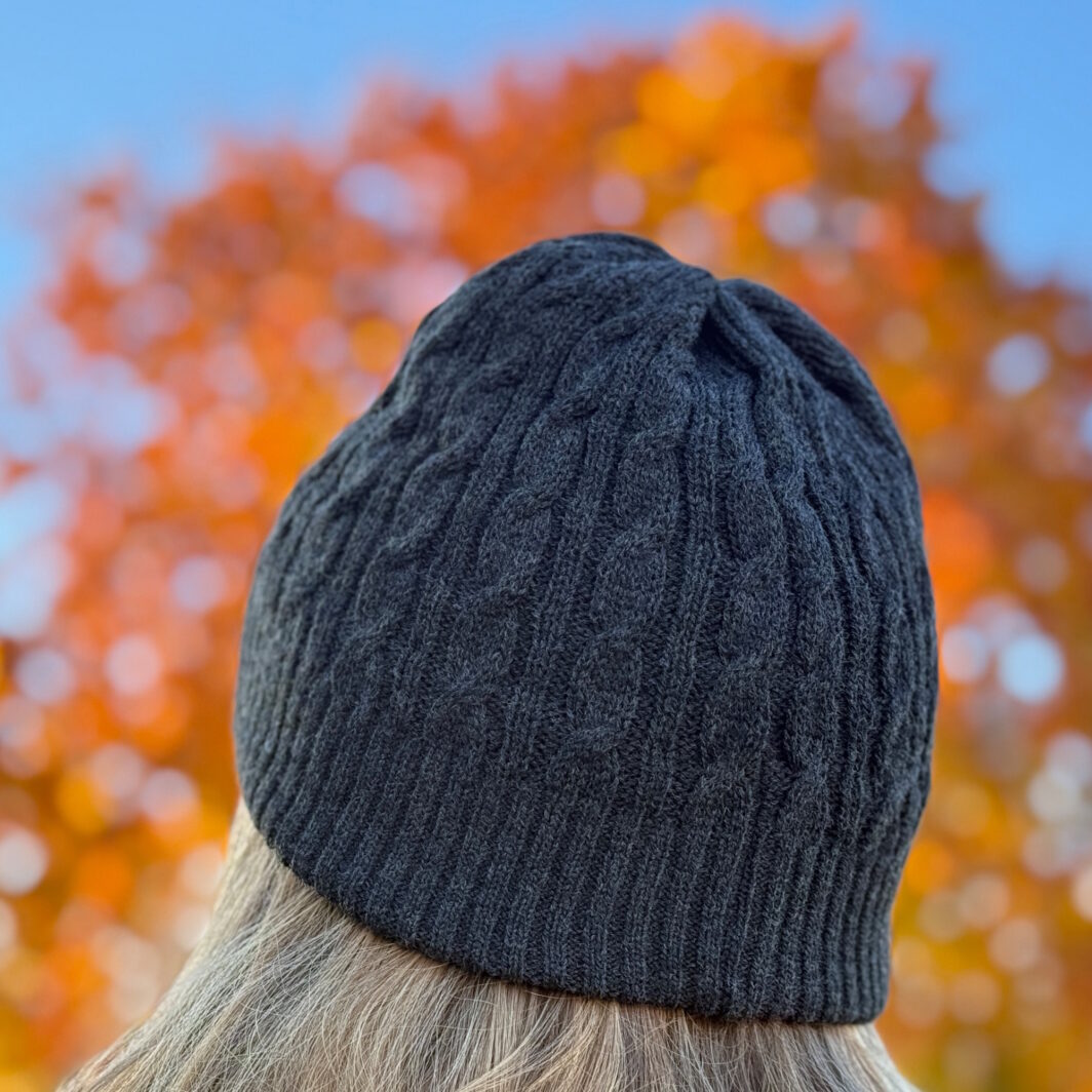 Mütze mit Zopfmuster im Herbst vor buntem Laub