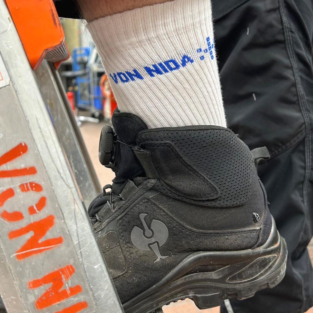 Handwerker-Fuß auf einer Leiter mit bedruckter Socke und Sicherheitsschuh