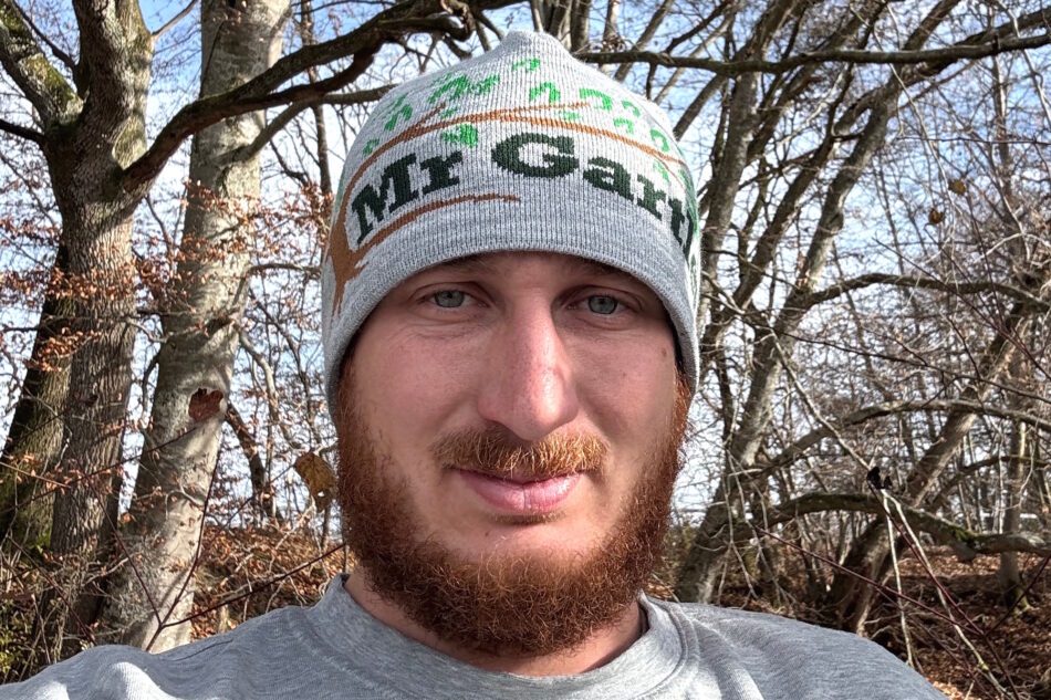 Mann mit Logo-Beanie vor Bäumen